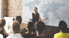 A woman is standing in front of a group of people, holding a laser pointer. She is standing in front of a map and giving a talk.