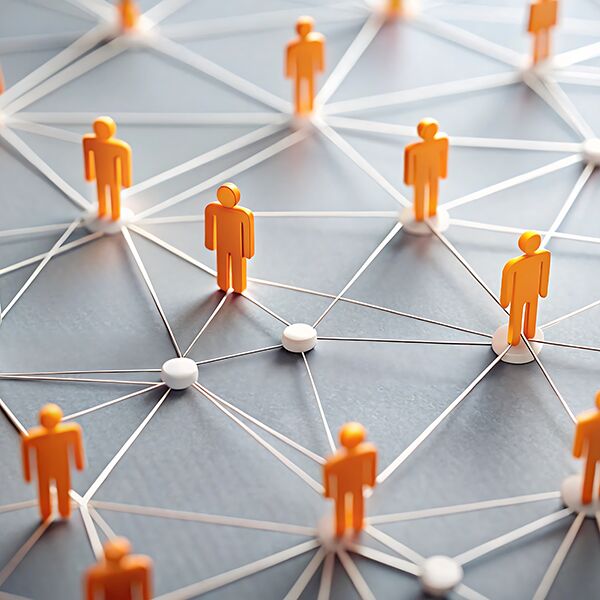 Ein Netz aus F&auml;den mit Knotenpunkten. Auf den Knotenpunkten stehen wei&szlig;e und orangene Holzfiguren.