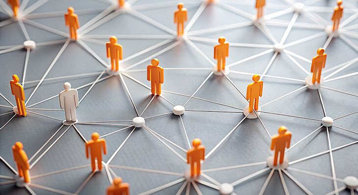 Ein Netz aus F&auml;den mit Knotenpunkten. Auf den Knotenpunkten stehen wei&szlig;e und orangene Holzfiguren.