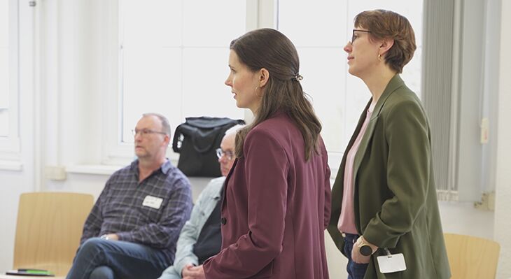 Zwei Moderatorinnen und Teilnehmende der VET Chain betrachten in einem Raum die Workshop-Materialien