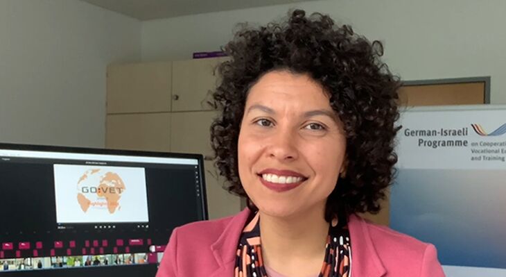 Aline at her work desk and she is smiling into the camera - in the background you can can see a glimpse of the editing process of our GOVET annual video 2024