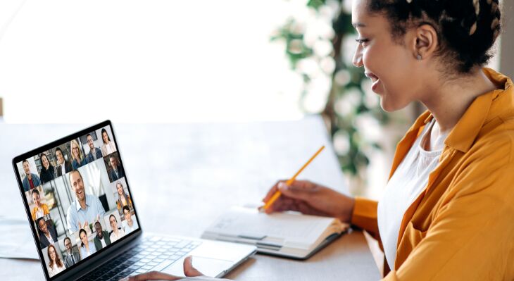junge Frau sitzt vor ihrem Laptop und nimmt an einer Videokonferenz teil, Infos zum Webinar als Overlay, Infos siehe Beitrag