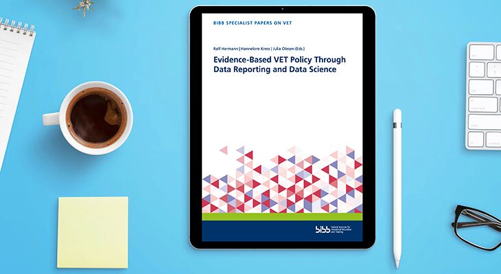 Ein Tablet liegt auf einem blauen Schreibtisch. Auf dem Tabletbildschirm ist die Publikation „Evidence-Based VET Policy Through Data Reporting and Data Science“  ge&ouml;ffnet